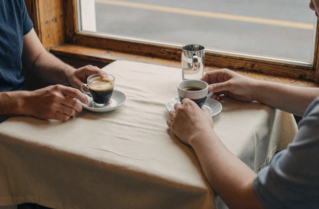 Two people at a small café table with espresso cups in warm afternoon light - companion essay on first dates