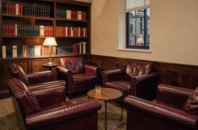 Warm members-club lounge with burgundy leather armchairs and a brass reading lamp - companion page for the Small Penis Club